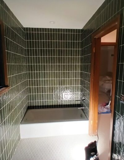 A bathroom with green tiled walls and a window.