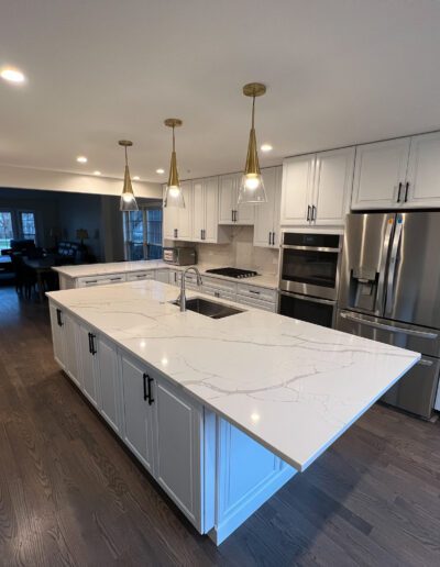 A white kitchen with marble counter tops and stainless steel appliances.